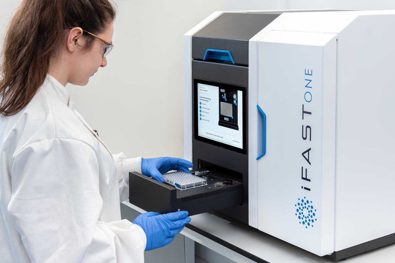 Scientist loading a sample plate into the iFAST ONE automated diagnostic system
